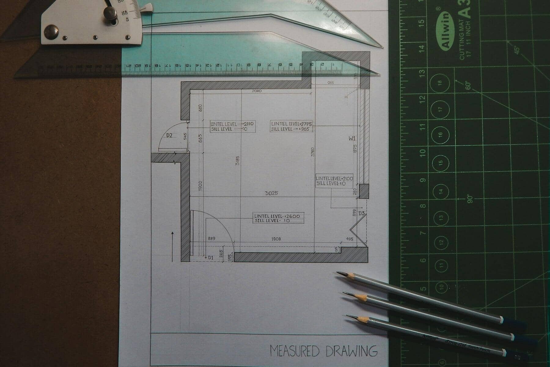 A pencil floor plan sketch on a cutting mat with a set square